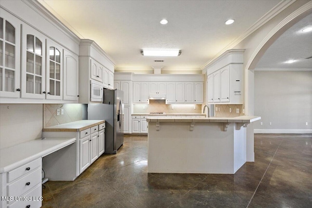 kitchen featuring white microwave, white cabinetry, ornamental molding, a kitchen bar, and glass insert cabinets