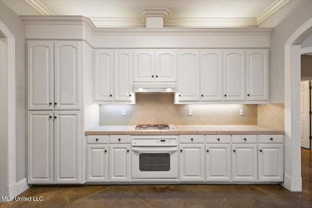 kitchen with white appliances, tile countertops, crown molding, under cabinet range hood, and white cabinetry