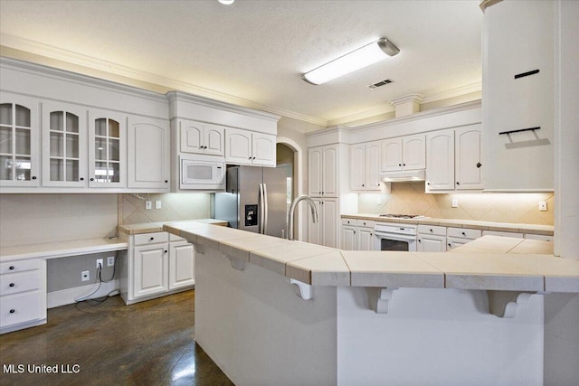 kitchen featuring ornamental molding, white appliances, a peninsula, a kitchen bar, and under cabinet range hood