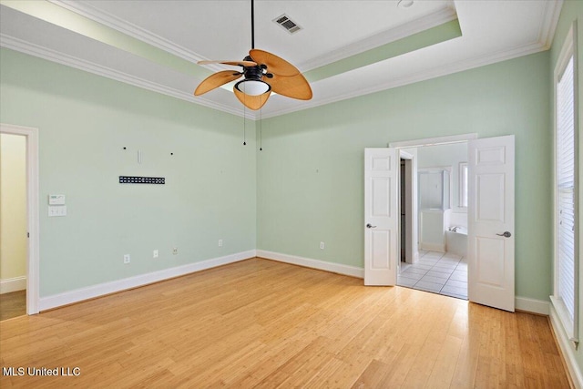 unfurnished bedroom featuring crown molding, light wood finished floors, a raised ceiling, visible vents, and baseboards