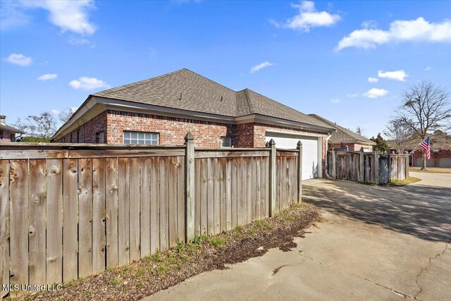 view of property exterior with a shingled roof, concrete driveway, an attached garage, fence, and brick siding