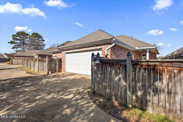 view of property exterior featuring concrete driveway, brick siding, a shingled roof, and fence