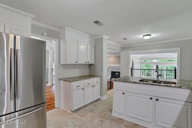 kitchen with ornamental molding, white cabinets, sink, and stainless steel refrigerator