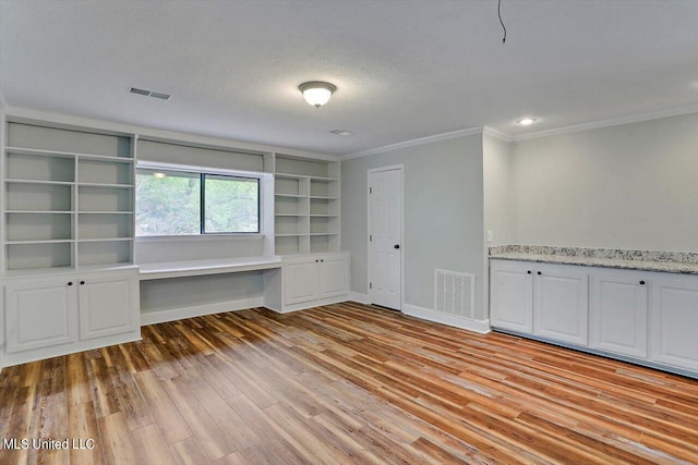 interior space featuring light hardwood / wood-style flooring, ornamental molding, built in desk, and a textured ceiling