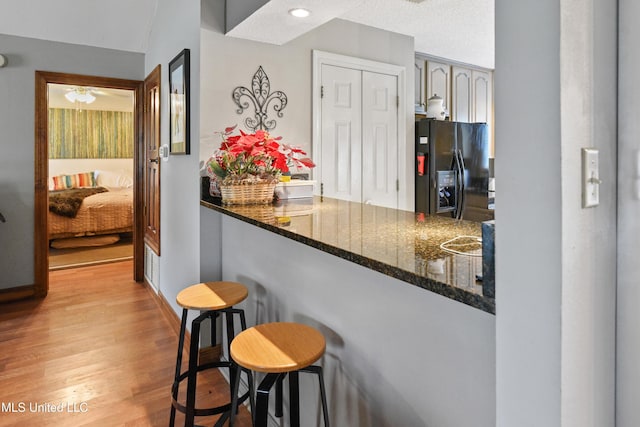 kitchen with kitchen peninsula, a kitchen breakfast bar, black fridge, dark stone counters, and light hardwood / wood-style flooring