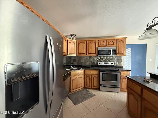 kitchen featuring light tile patterned floors, a sink, appliances with stainless steel finishes, dark countertops, and brown cabinets