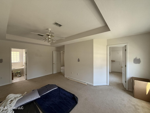 bedroom with baseboards, visible vents, a tray ceiling, light carpet, and connected bathroom