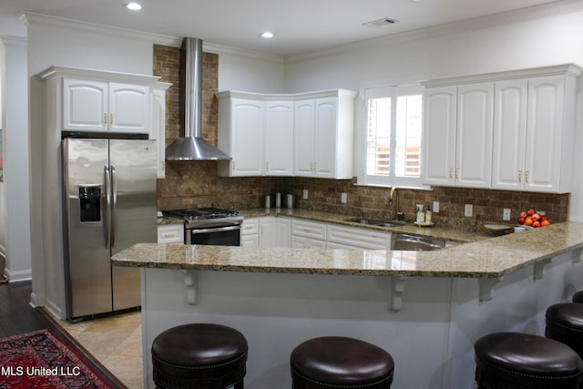 kitchen featuring white cabinetry, wall chimney exhaust hood, appliances with stainless steel finishes, and a kitchen breakfast bar