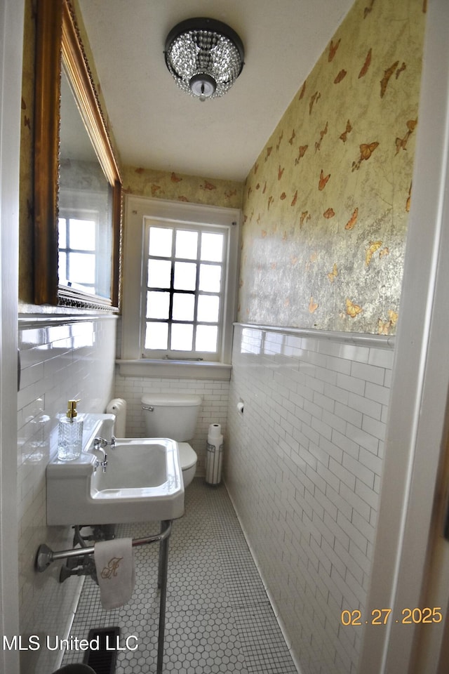 half bathroom featuring a wealth of natural light, tile patterned flooring, a wainscoted wall, and wallpapered walls