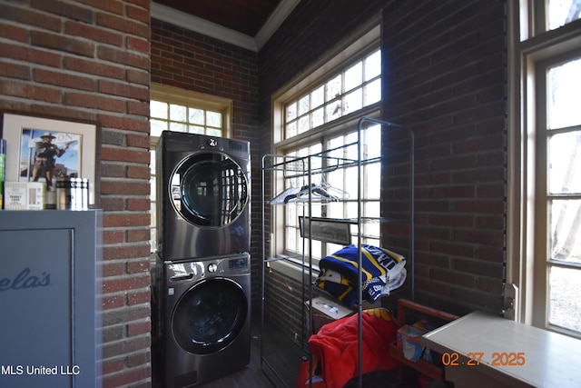 laundry room featuring ornamental molding, brick wall, and stacked washing maching and dryer