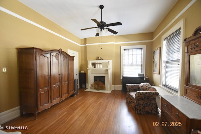 living area featuring a fireplace with flush hearth, baseboards, ceiling fan, and wood finished floors