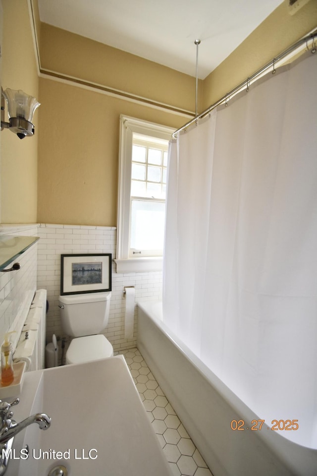 bathroom featuring a wainscoted wall, tile walls, toilet, shower / bath combo, and tile patterned floors