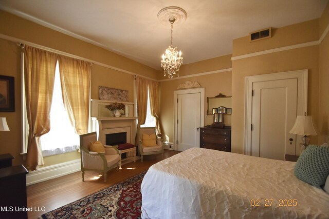 bedroom with dark wood finished floors, visible vents, an inviting chandelier, a brick fireplace, and baseboards