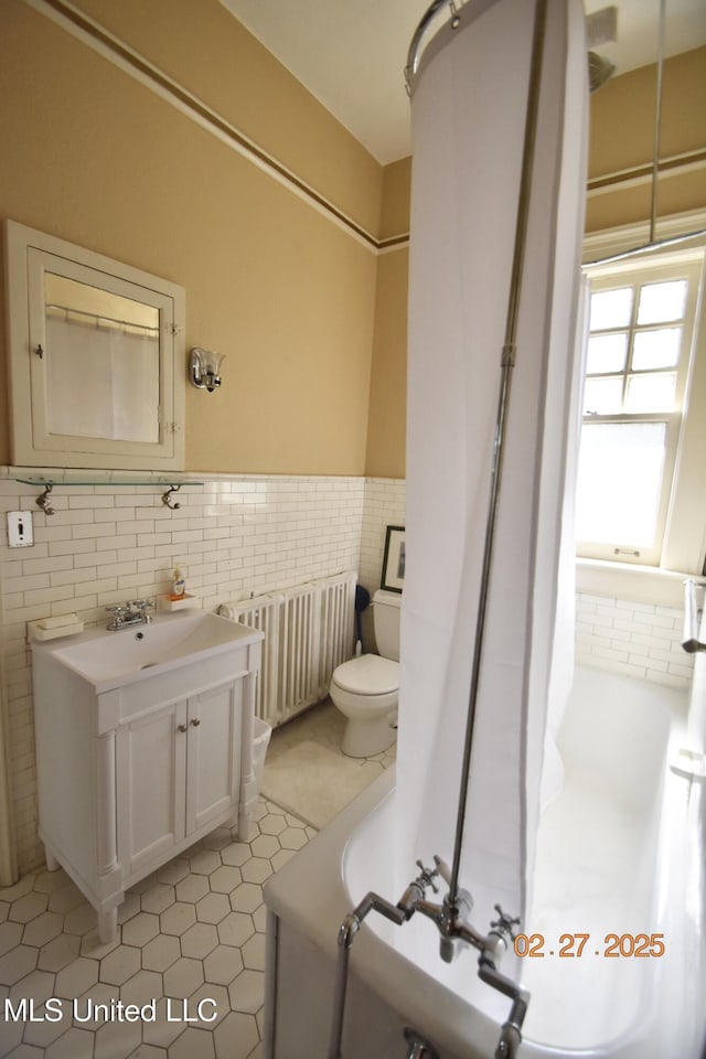 full bathroom with a wainscoted wall, tile walls, toilet, radiator heating unit, and vanity