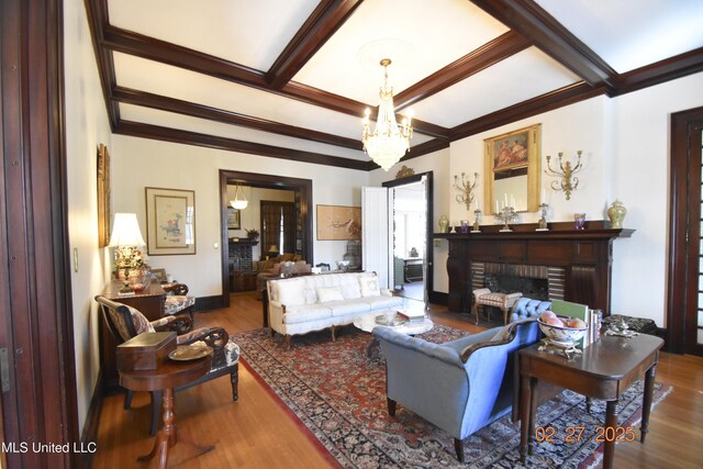 living area featuring beam ceiling, crown molding, a notable chandelier, a brick fireplace, and wood finished floors