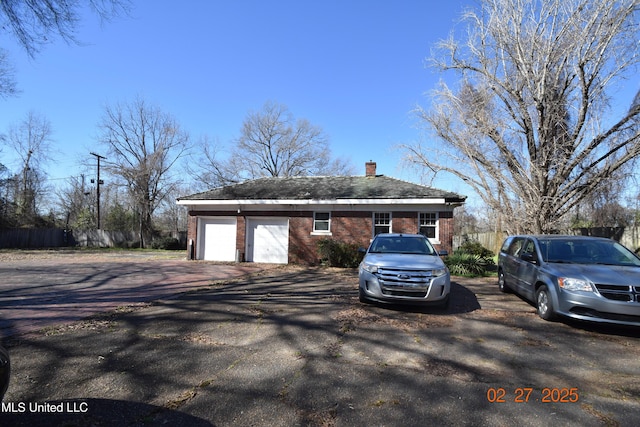 view of front of home featuring a garage, brick siding, fence, and a chimney