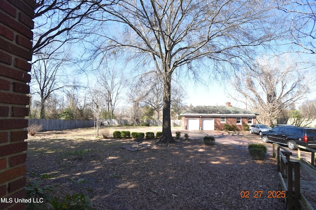 exterior space with driveway, a garage, a chimney, fence, and brick siding