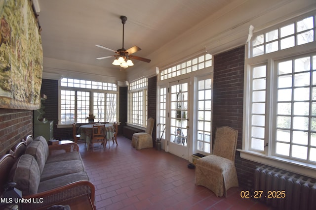 living room featuring radiator, brick floor, a ceiling fan, and crown molding