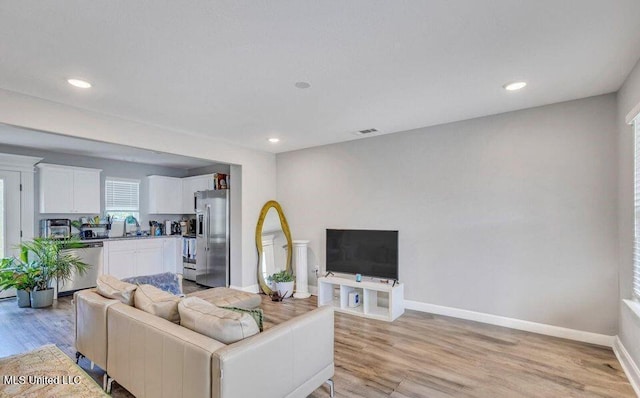 living area with light wood finished floors, recessed lighting, visible vents, and baseboards