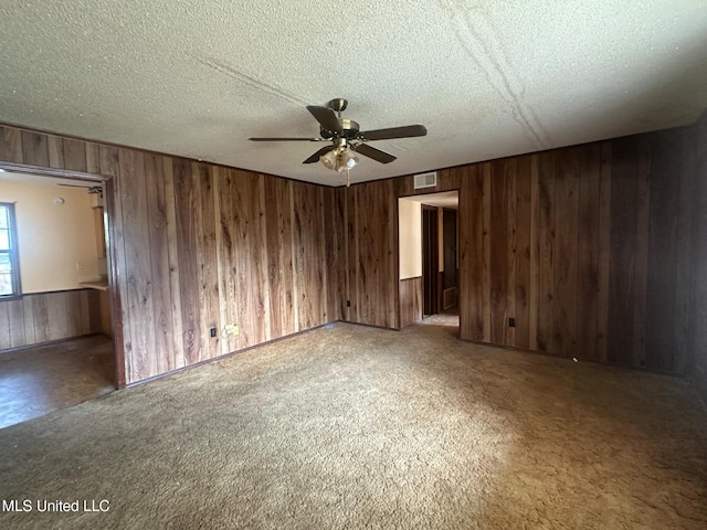 carpeted empty room featuring ceiling fan, a textured ceiling, and wood walls