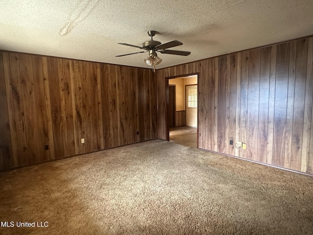 spare room with ceiling fan, carpet flooring, a textured ceiling, and wood walls