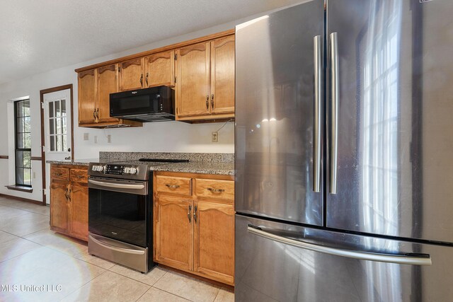 7300 Frank Snell Rd, Moss Point, MS 39562 - kitchen featuring stainless steel appliances, brown cabinetry, light tile patterned flooring, and dark stone countertops