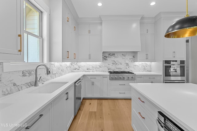 kitchen with sink, light wood-type flooring, hanging light fixtures, stainless steel appliances, and white cabinets