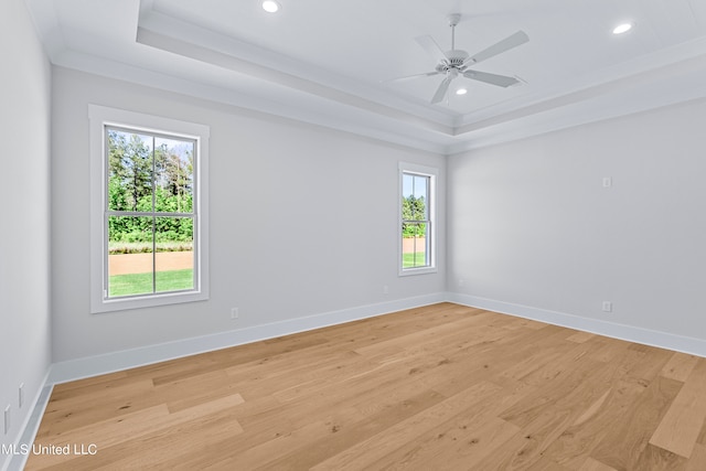 empty room with crown molding, light hardwood / wood-style flooring, ceiling fan, and a raised ceiling