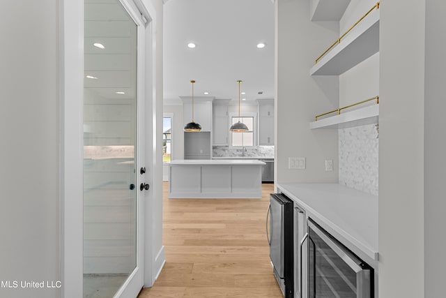 kitchen featuring tasteful backsplash, dishwasher, hanging light fixtures, beverage cooler, and light hardwood / wood-style flooring