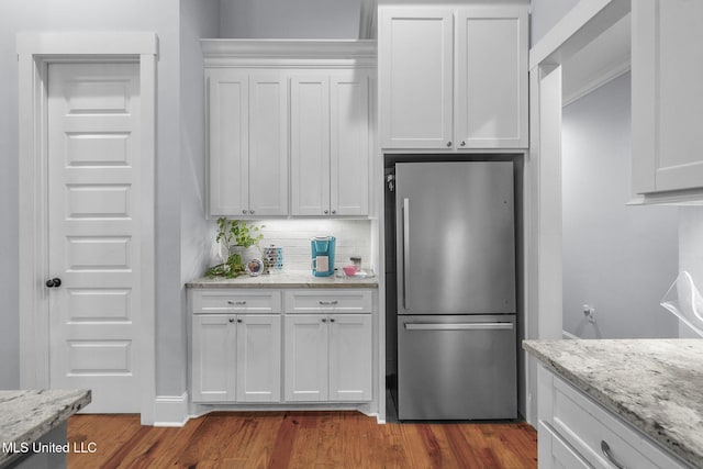 kitchen with light stone counters, stainless steel refrigerator, hardwood / wood-style flooring, decorative backsplash, and white cabinets