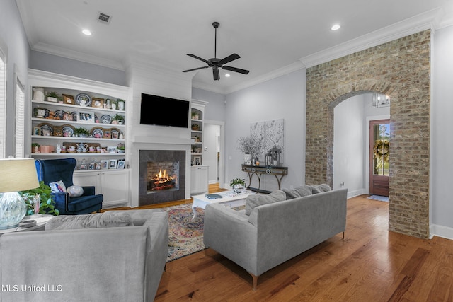 living room featuring built in shelves, wood-type flooring, ornamental molding, and ceiling fan