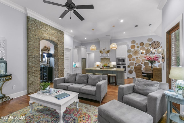 living room featuring wood-type flooring, sink, ceiling fan with notable chandelier, and crown molding