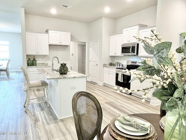 15681 Perdido Dr, Gulfport, MS 39503 - kitchen featuring stainless steel appliances, white cabinetry, a center island with sink, light wood-style floors, and recessed lighting