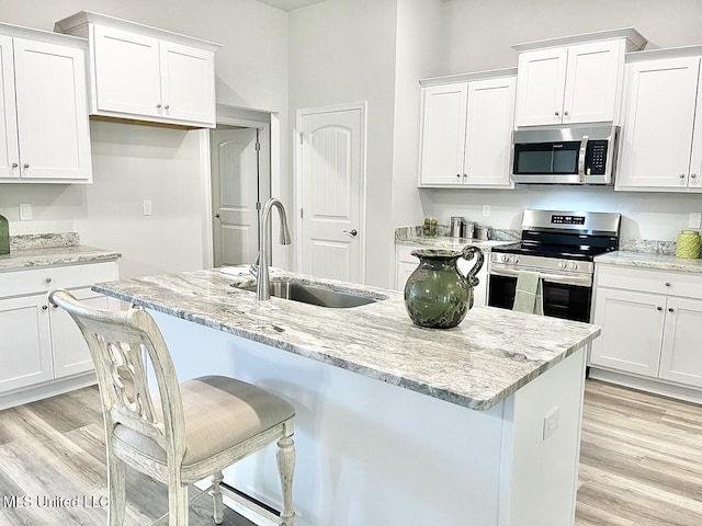15681 Perdido Dr, Gulfport, MS 39503 - kitchen featuring appliances with stainless steel finishes, a sink, white cabinetry, light wood finished floors, and light stone counters
