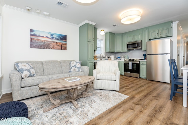 living area featuring ornamental molding, light wood-style flooring, and visible vents