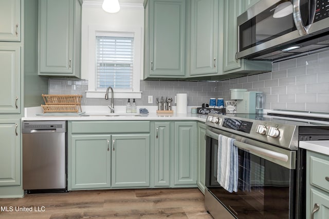 kitchen featuring green cabinets, a sink, decorative backsplash, light wood-style floors, and stainless steel appliances