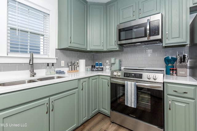 kitchen with a sink, green cabinetry, light countertops, appliances with stainless steel finishes, and decorative backsplash