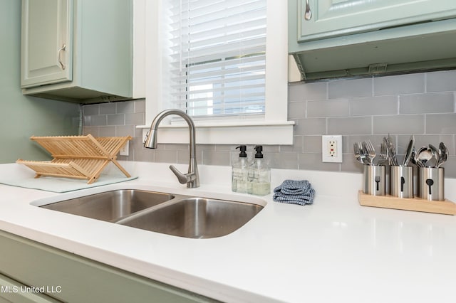 room details with light countertops, green cabinetry, decorative backsplash, and a sink