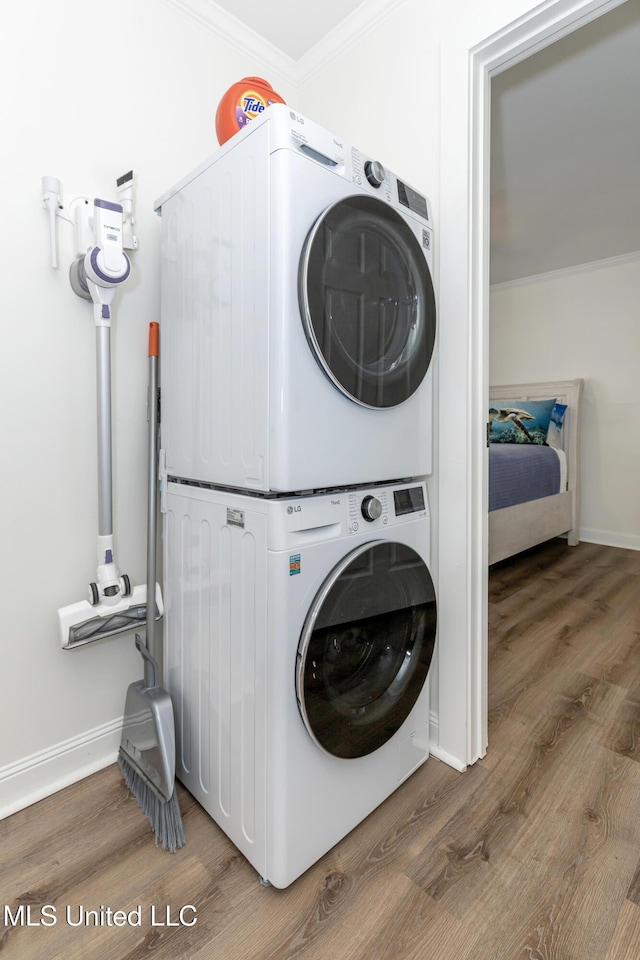 laundry room featuring stacked washer and clothes dryer, wood finished floors, baseboards, and ornamental molding