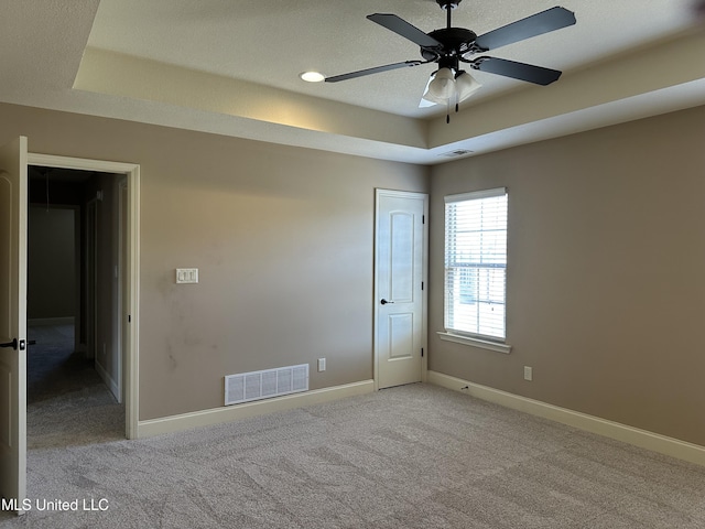 carpeted empty room with a raised ceiling, visible vents, and baseboards