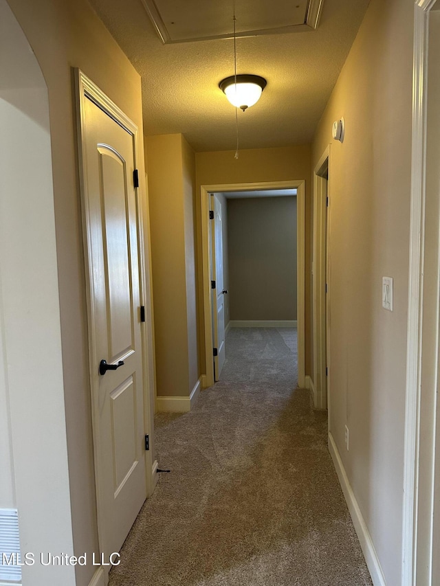 hallway featuring a textured ceiling, carpet flooring, attic access, and baseboards