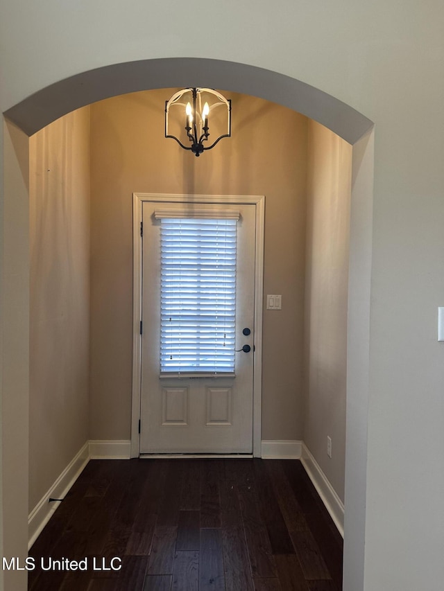 entryway with arched walkways, dark wood-style flooring, a chandelier, and baseboards