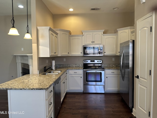 kitchen with dark wood-style floors, appliances with stainless steel finishes, a sink, light stone countertops, and a peninsula