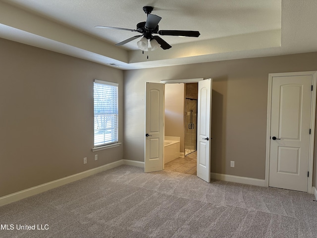 unfurnished bedroom with a textured ceiling, carpet, a raised ceiling, and baseboards