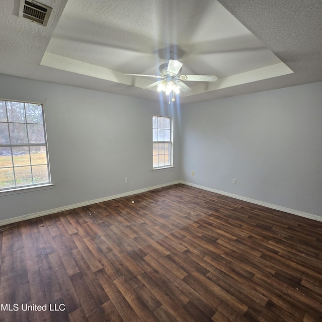 empty room featuring ceiling fan, dark wood-type flooring, a textured ceiling, and a tray ceiling