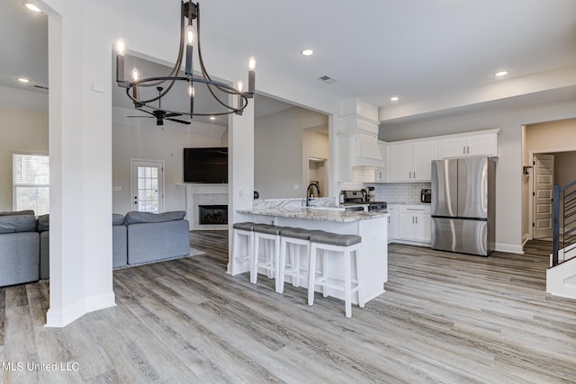 kitchen with kitchen peninsula, white cabinets, light stone countertops, light hardwood / wood-style floors, and stainless steel appliances