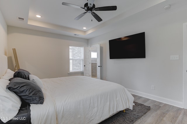 bedroom featuring ceiling fan, a raised ceiling, and light wood-type flooring