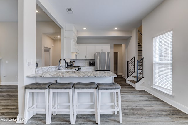 kitchen featuring backsplash, kitchen peninsula, white cabinetry, light stone counters, and stainless steel refrigerator