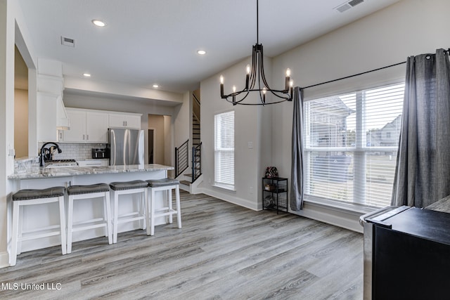 kitchen featuring white cabinetry, a healthy amount of sunlight, light wood-type flooring, and stainless steel fridge