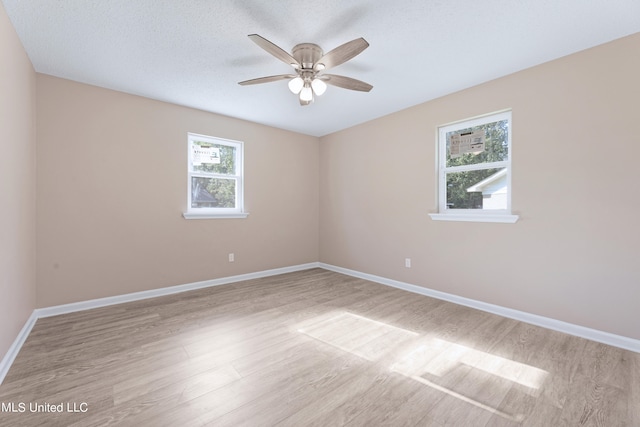 empty room featuring a wealth of natural light, a textured ceiling, light wood-type flooring, and ceiling fan